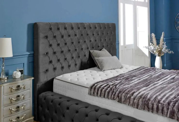 Gray tufted bed with matching headboard and bench against a blue wall.