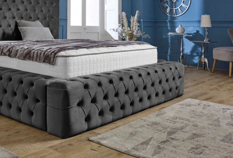 Gray tufted bed in a bedroom with blue walls and decorative elements.