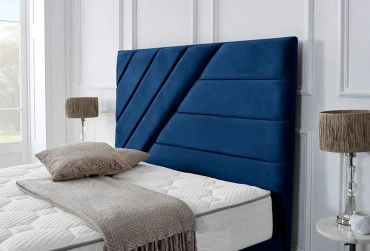 Blue upholstered headboard on a bed with white mattress and gray bedding in a room with white walls and a window.