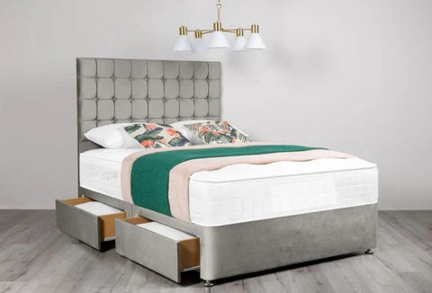 Gray upholstered bed with floral bedding and green blanket in a room with a chandelier.