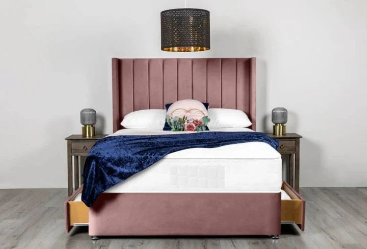 Pink upholstered bed with white bedding and a blue throw blanket in a room setting.