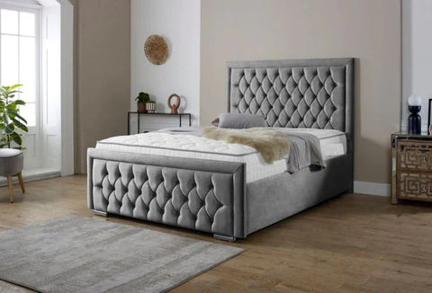 Gray tufted bed in a room with wooden flooring and a plant.